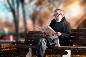 man reading newspaper on park bench